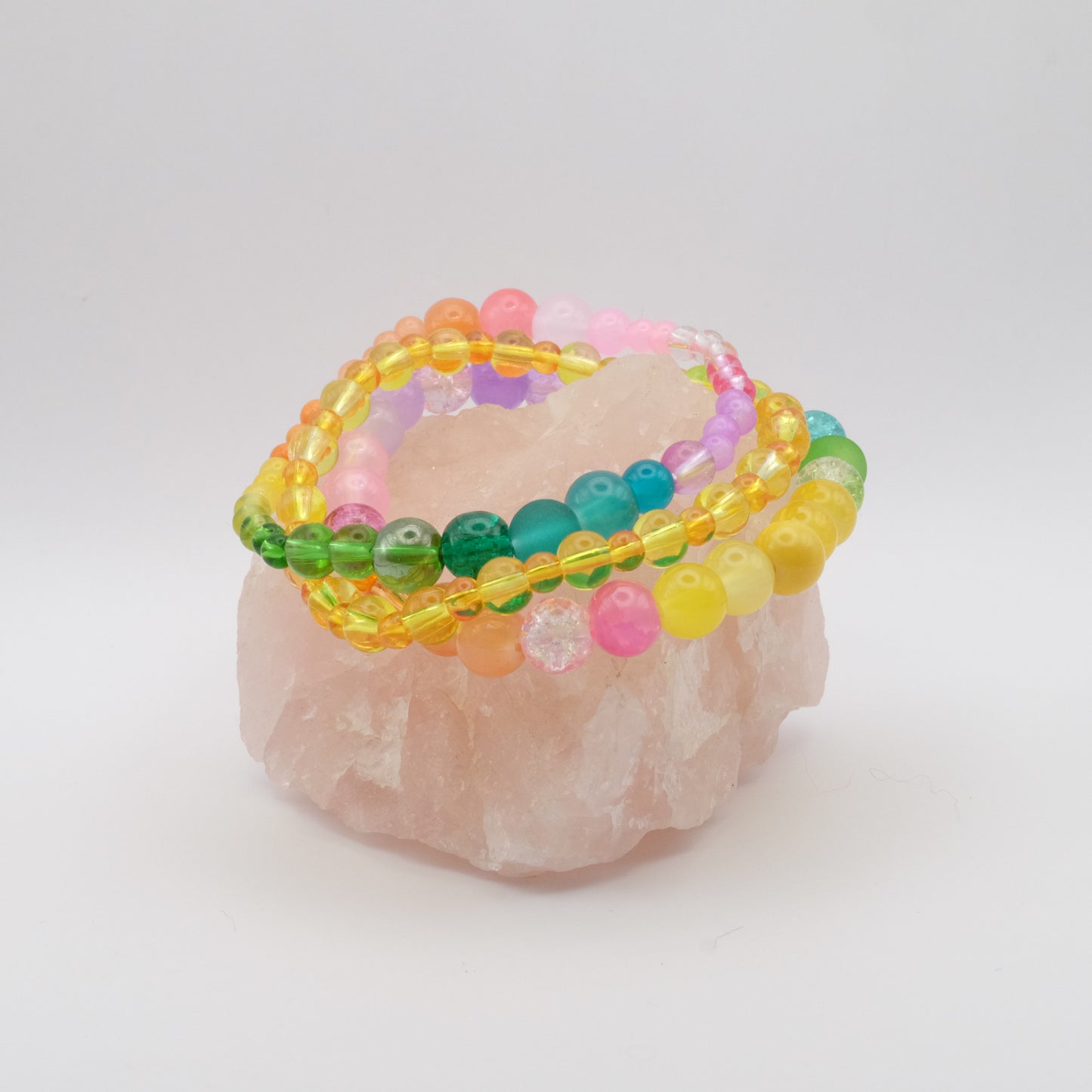 A stack of three elastic beaded bracelets in the colours of the rainbow sitting on a rose quartz rock.