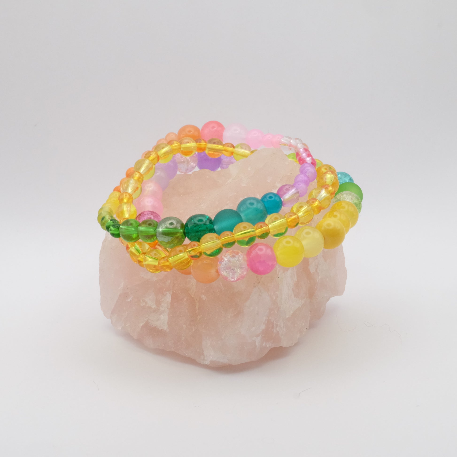 A stack of three elastic beaded bracelets in the colours of the rainbow sitting on a rose quartz rock.