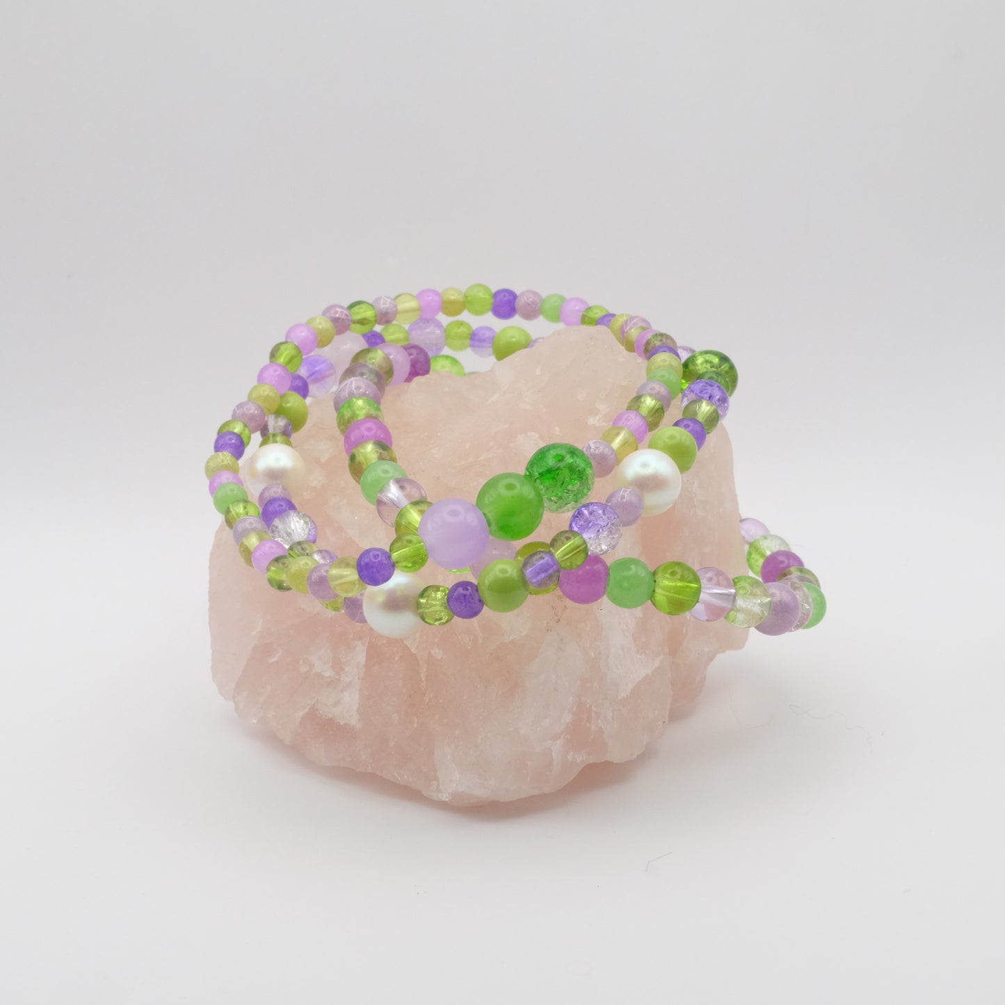 Three elastic beaded bracelets in green and purple on a pink stone with a white background