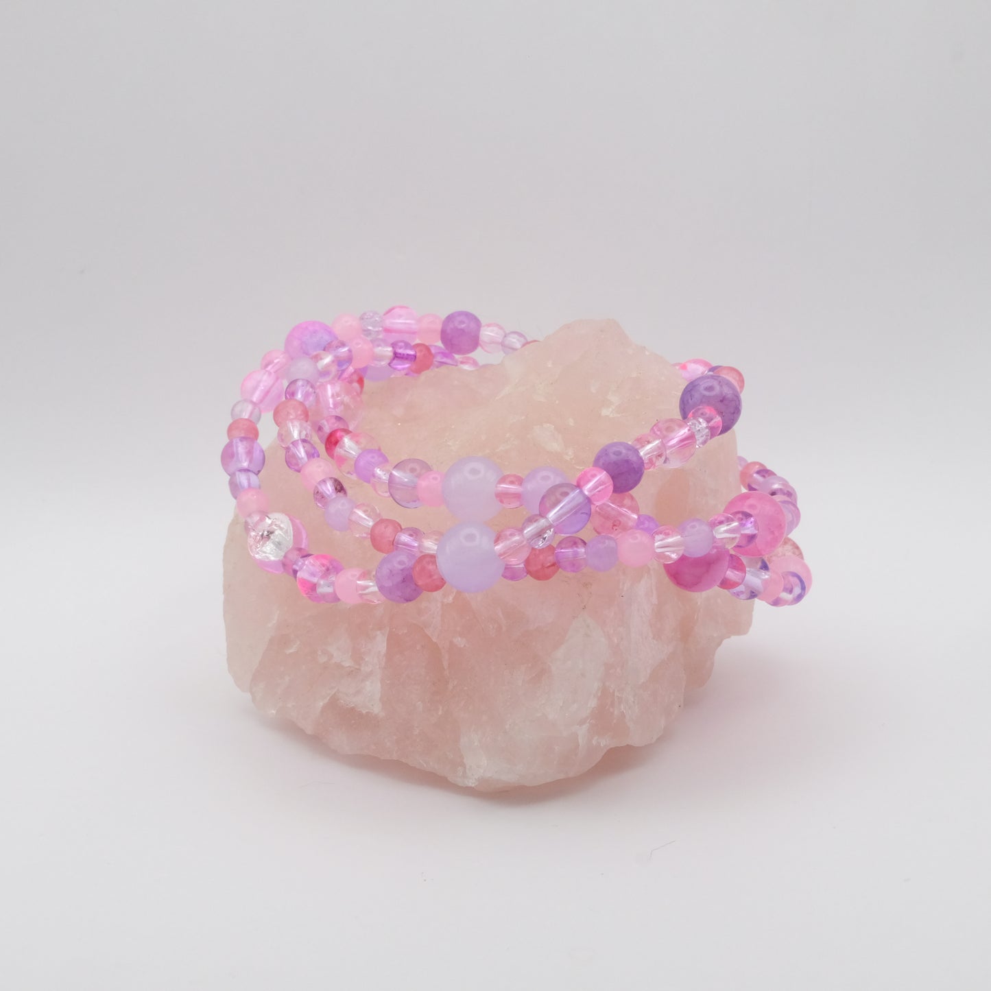 A stack of three elastic beaded bracelets in pinks and purples sitting on a rose quartz rock.