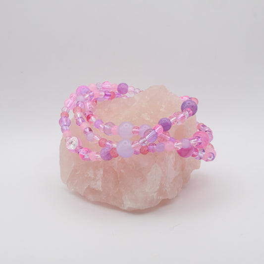 A stack of three elastic beaded bracelets in pinks and purples sitting on a rose quartz rock.