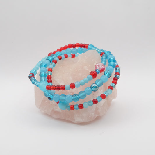 Turquoise and red beaded bracelets on a pink stone with a white background