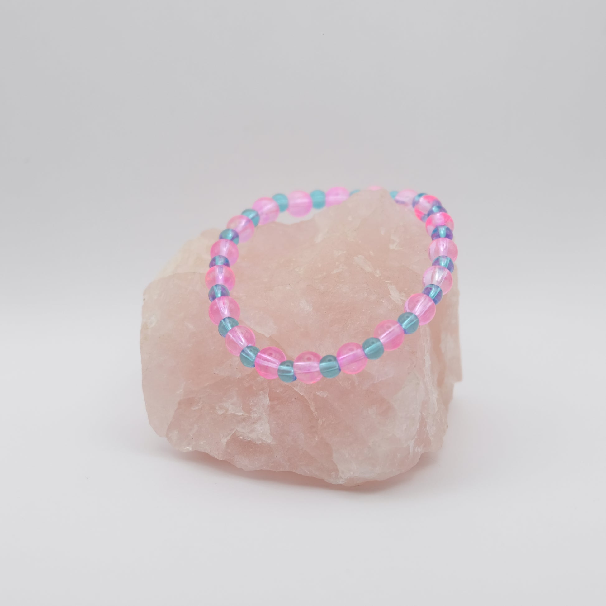 Beaded bracelet with pink and blue beads on a rock against a white background