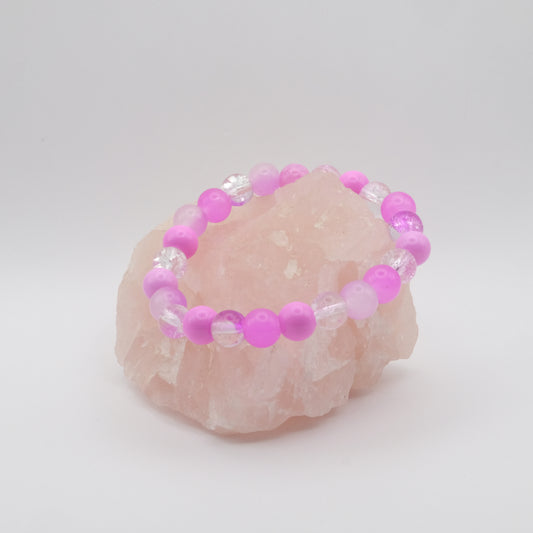 A pinky purple elastic beaded bracelet sitting on a rose quartz rock with a white background