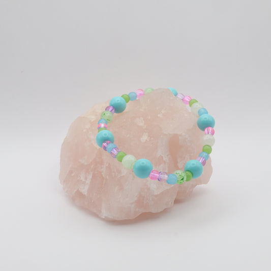 A single elastic beaded bracelet in pink, blue, purple and green sitting on a rose quartz rock with a white background