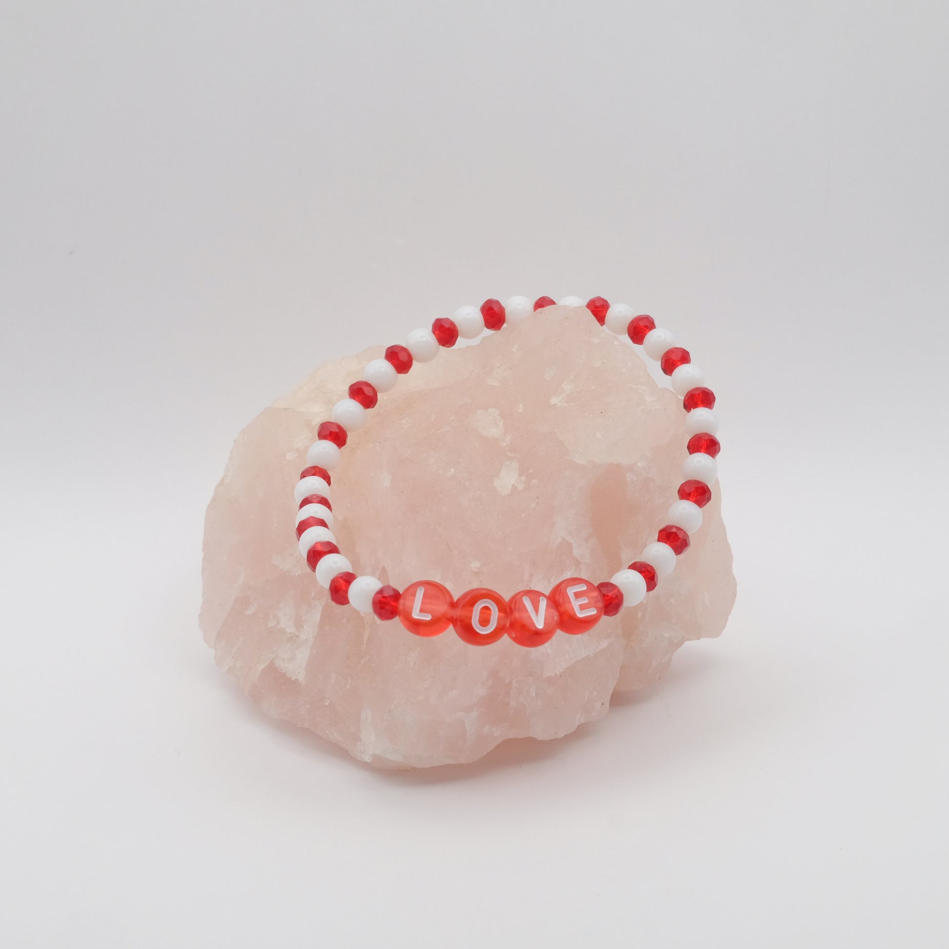 Red and white beaded bracelet with 'LOVE' on a pink stone against a white background