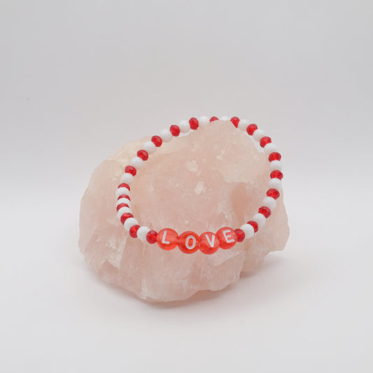 Red and white beaded bracelet with 'LOVE' on a pink stone against a white background