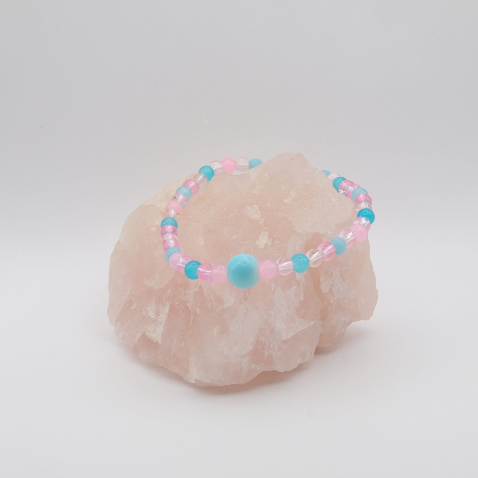 A single elastic beaded bracelet in pink and blue sitting on a rose quartz rock with a white background