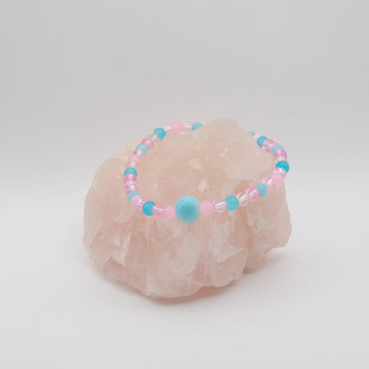 A single elastic beaded bracelet in pink and blue sitting on a rose quartz rock with a white background