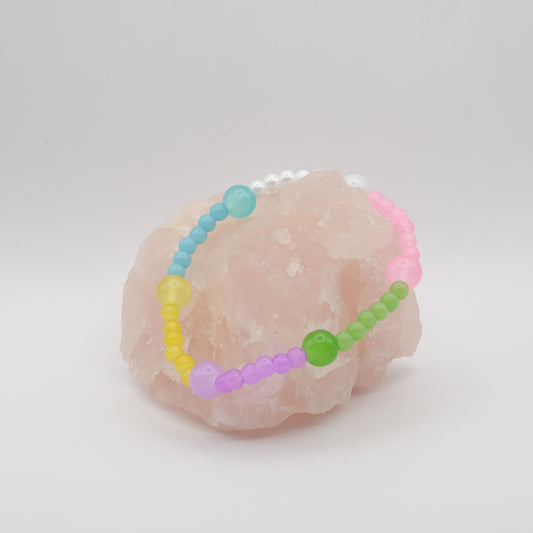 A single pastel coloured elastic beaded bracelet in pink, green, blue, purple, yellow and white sitting on a rose quartz rock with a white background
