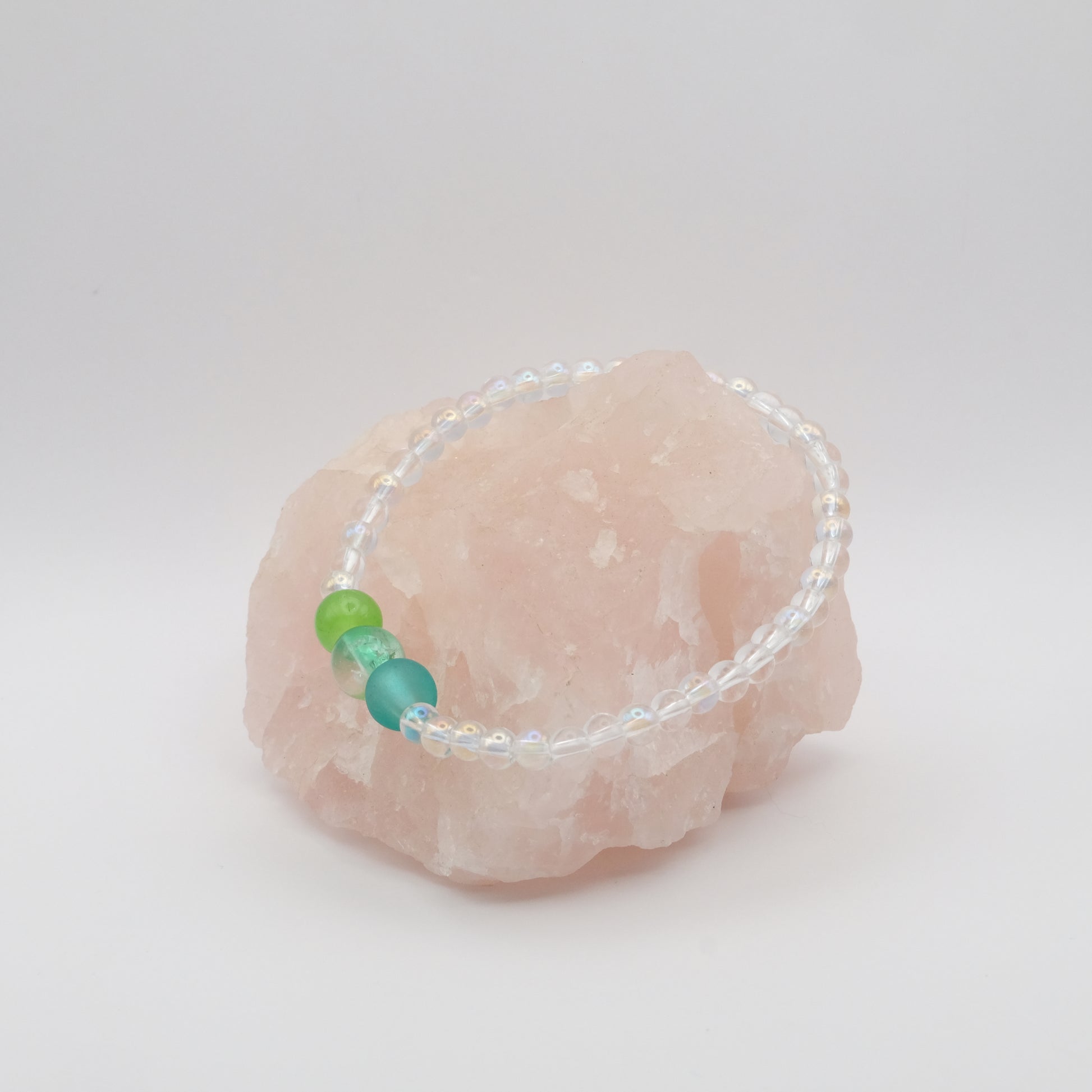 Bracelet with green and blue beads on a pink stone against a white background