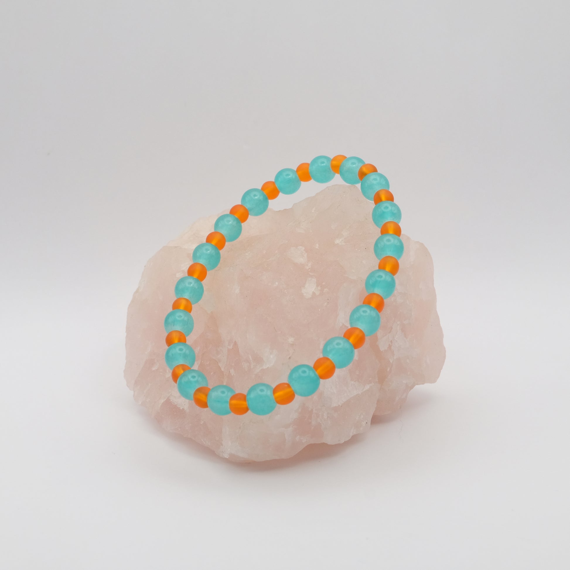 Turquoise and orange beaded bracelet on a pink stone with a white background