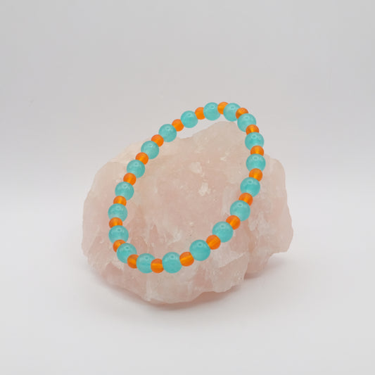 Turquoise and orange beaded bracelet on a pink stone with a white background
