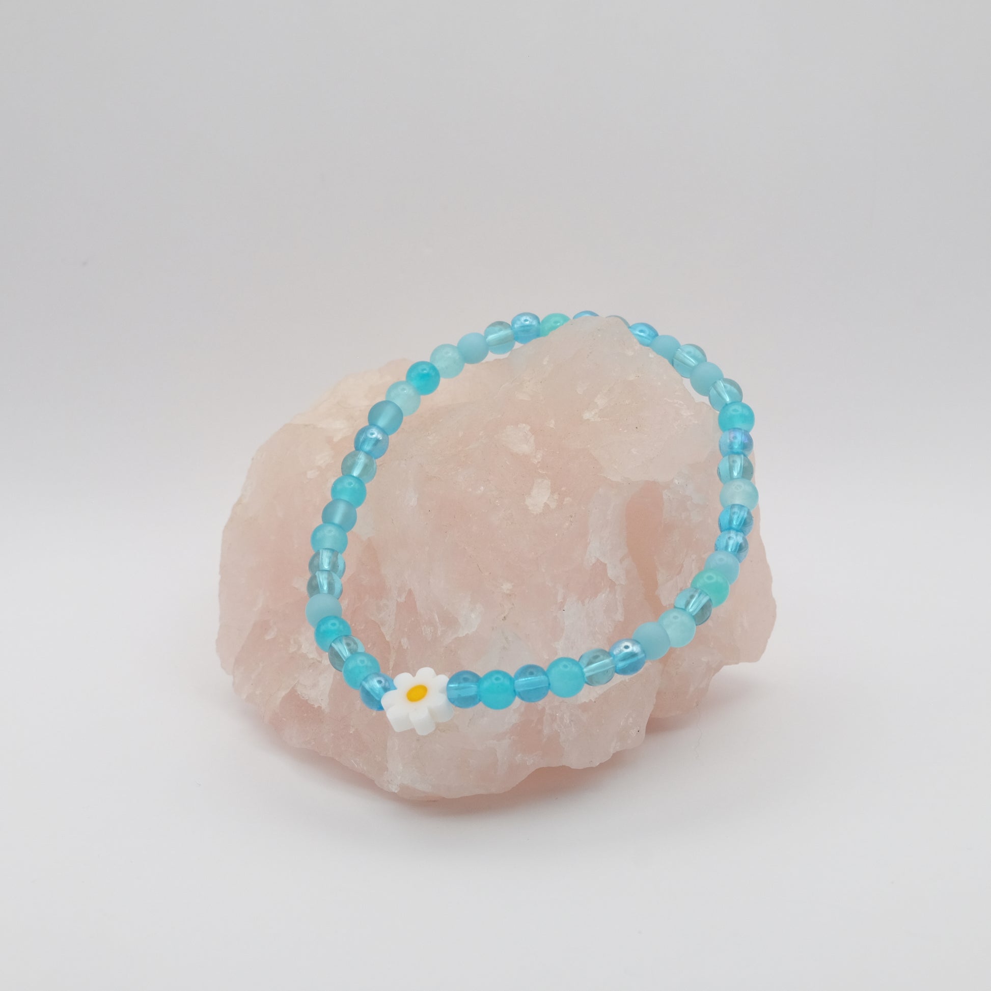 Turquoise beaded bracelet with a white flower charm on a pink stone.