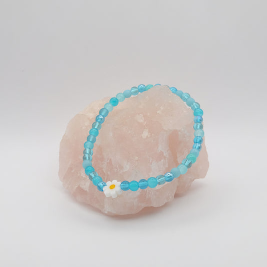 Turquoise beaded bracelet with a white flower charm on a pink stone.