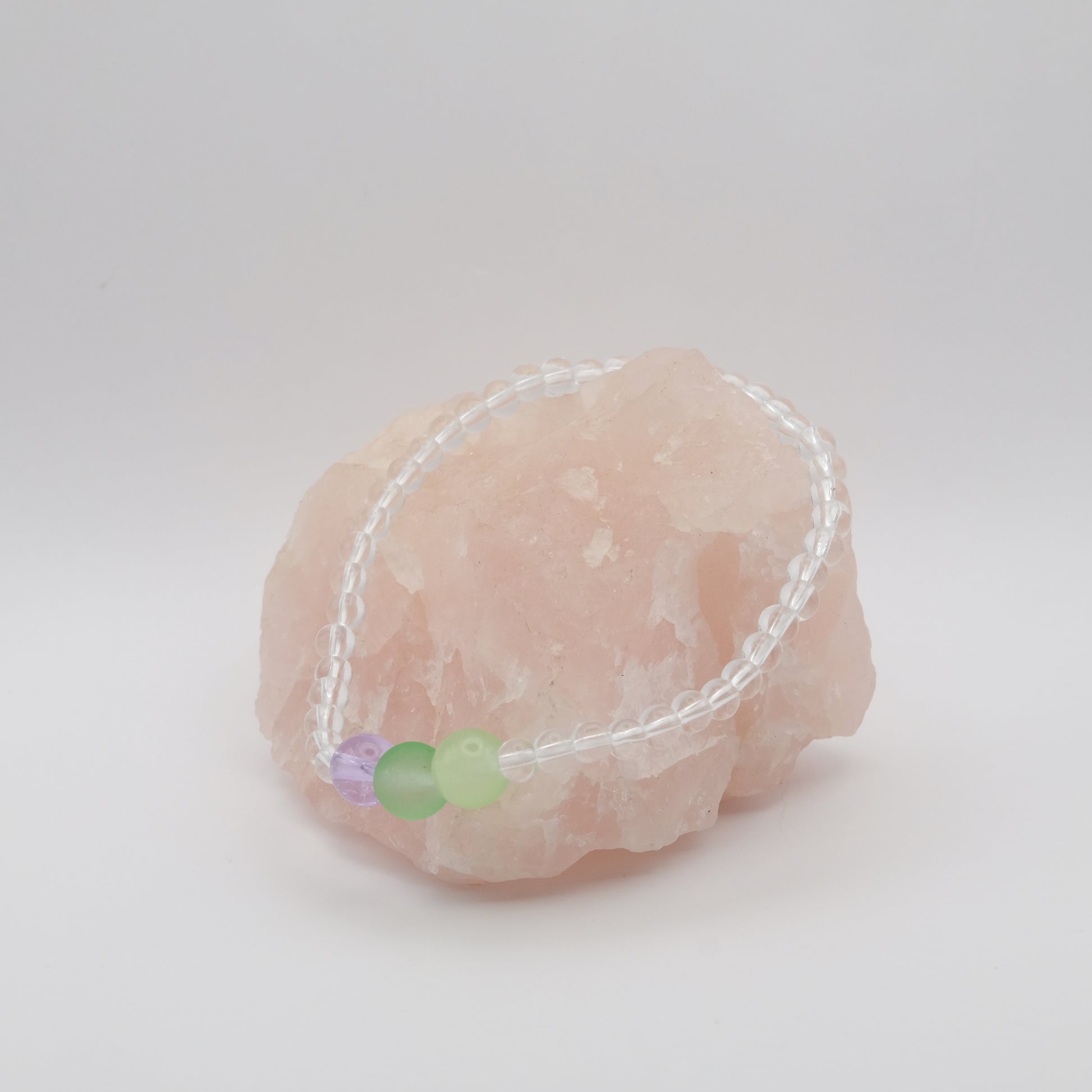 Bracelet with green and purple beads on a pink stone against a white background