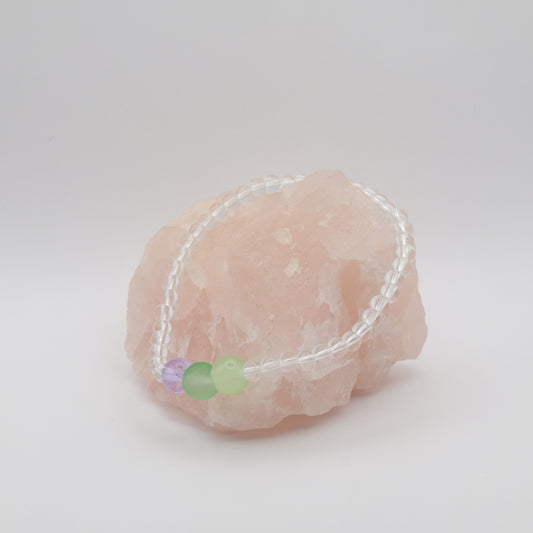 Bracelet with green and purple beads on a pink stone against a white background