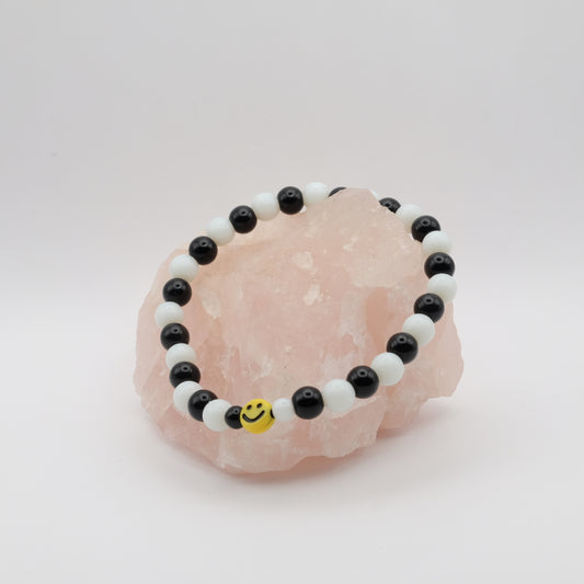 Black and white beaded bracelet with a smiley face charm on a pink crystal.