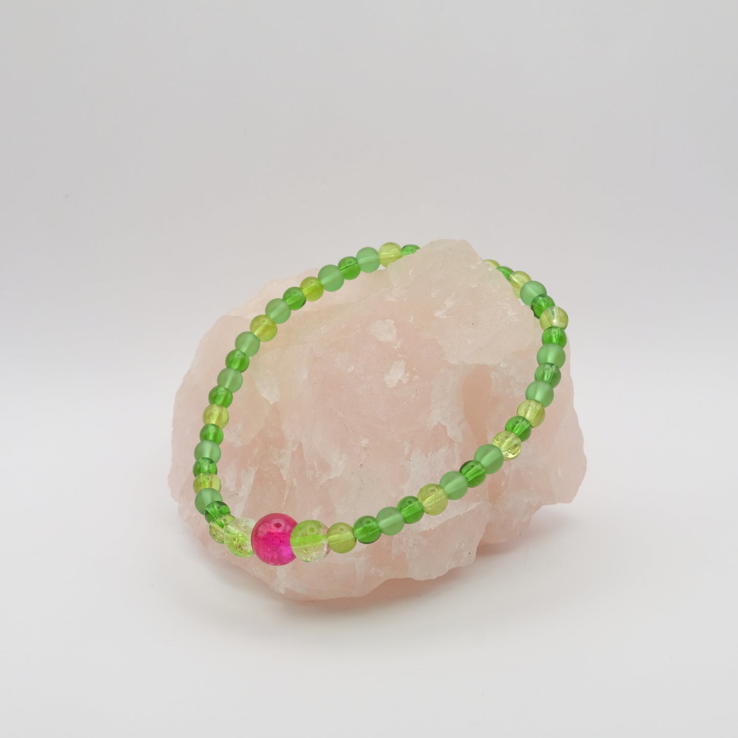 Green beaded bracelet with a pink bead on a white background