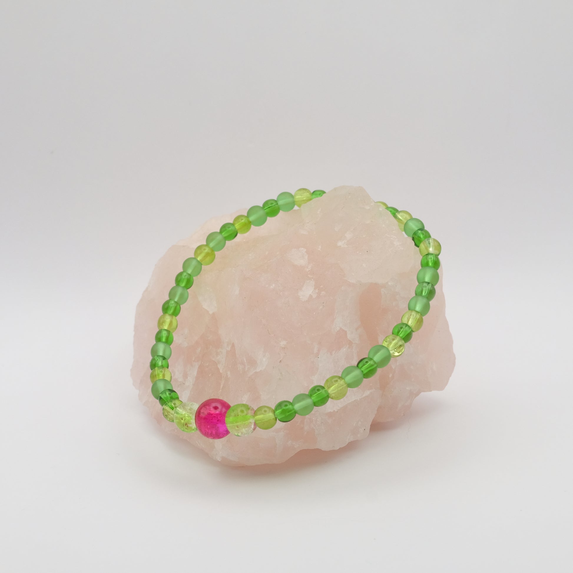 Green beaded bracelet with a pink bead on a white background