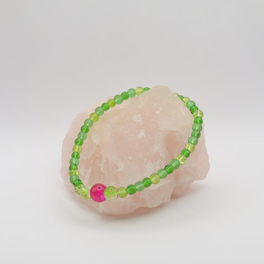 Green beaded bracelet with a pink bead on a white background