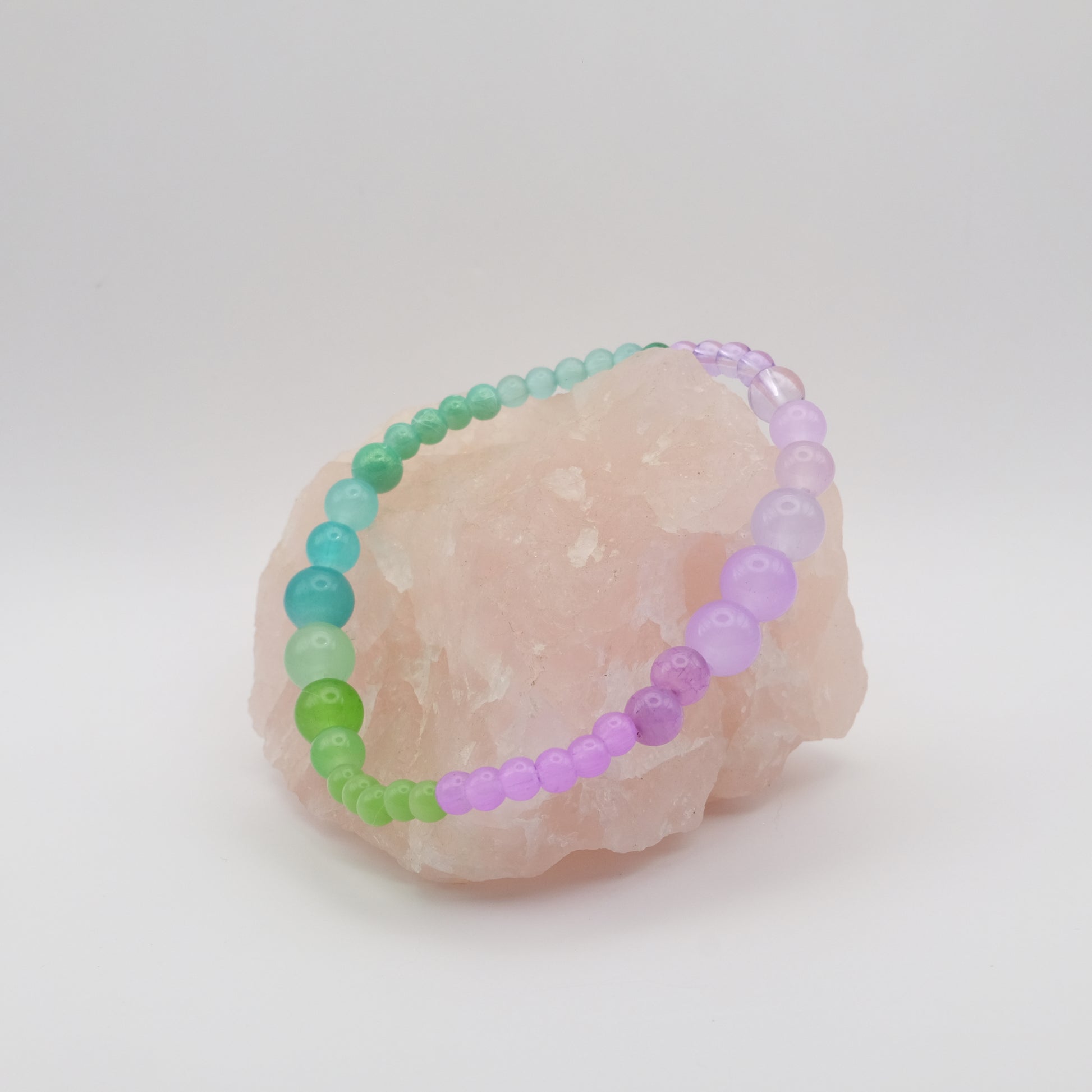 Beaded bracelet with green and purple beads on a stone surface