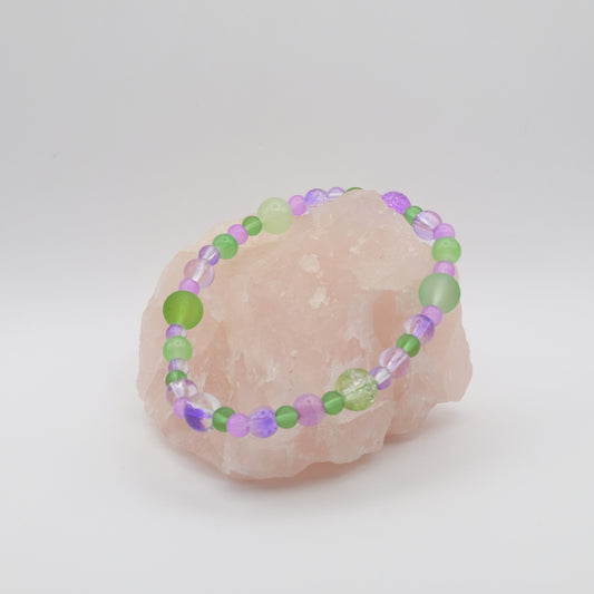 Beaded bracelet with green and purple beads on a pink stone against a white background