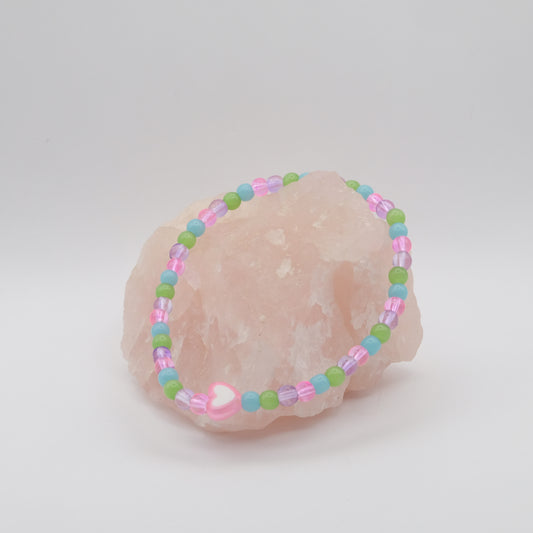 Pastel beaded bracelet on a seashell against a light gray background