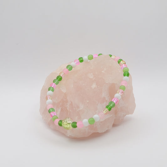 Beaded bracelet with green, pink, and white beads on a pink stone against a light gray background