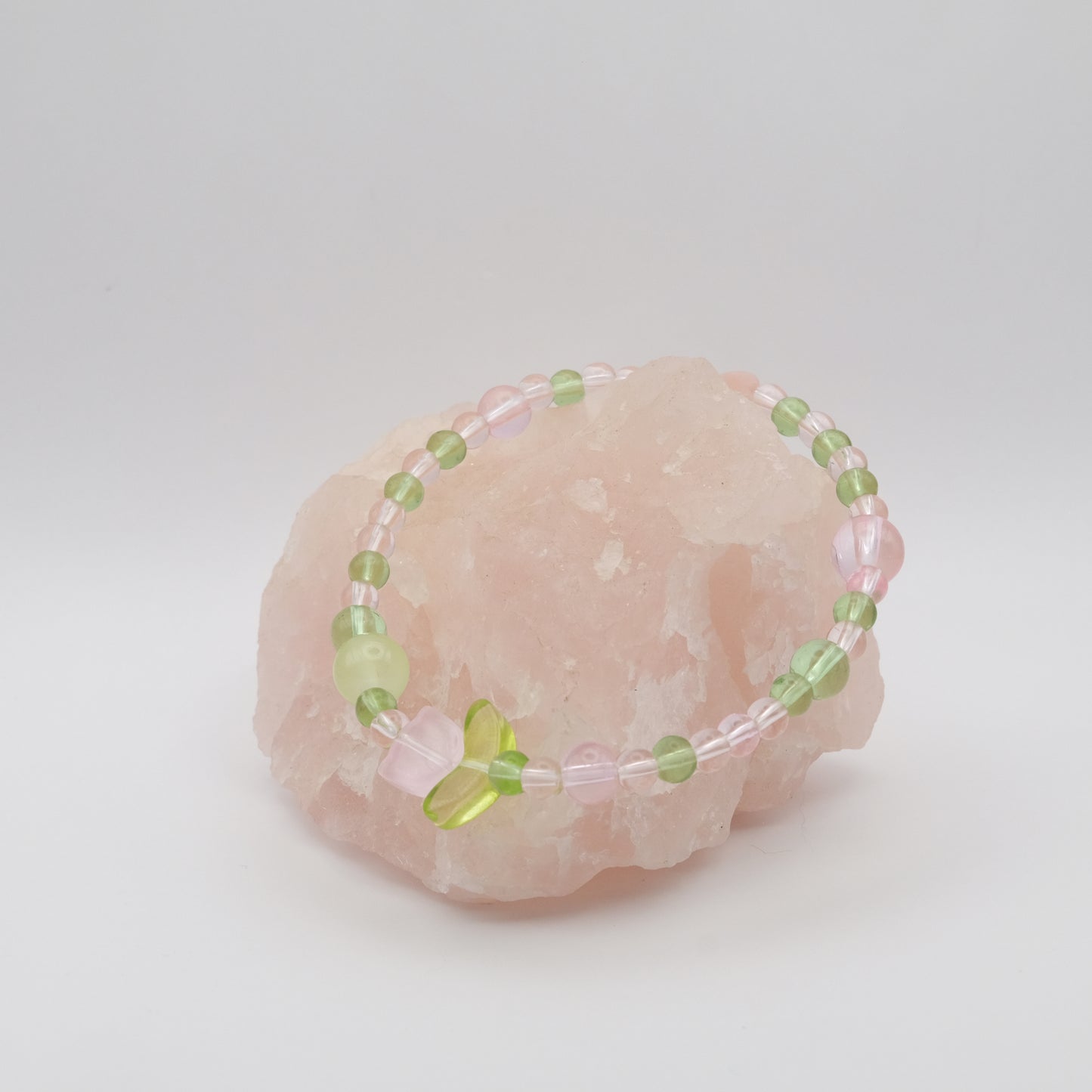 Beaded bracelet with green and pink beads on a pink stone against a white background