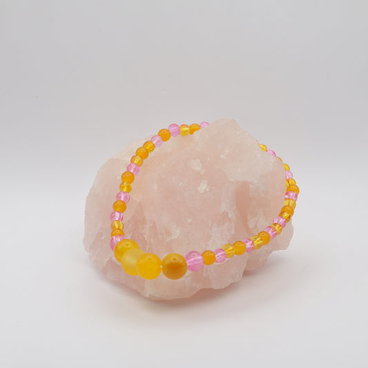 Beaded bracelet with yellow and pink beads on a pink stone with a white background