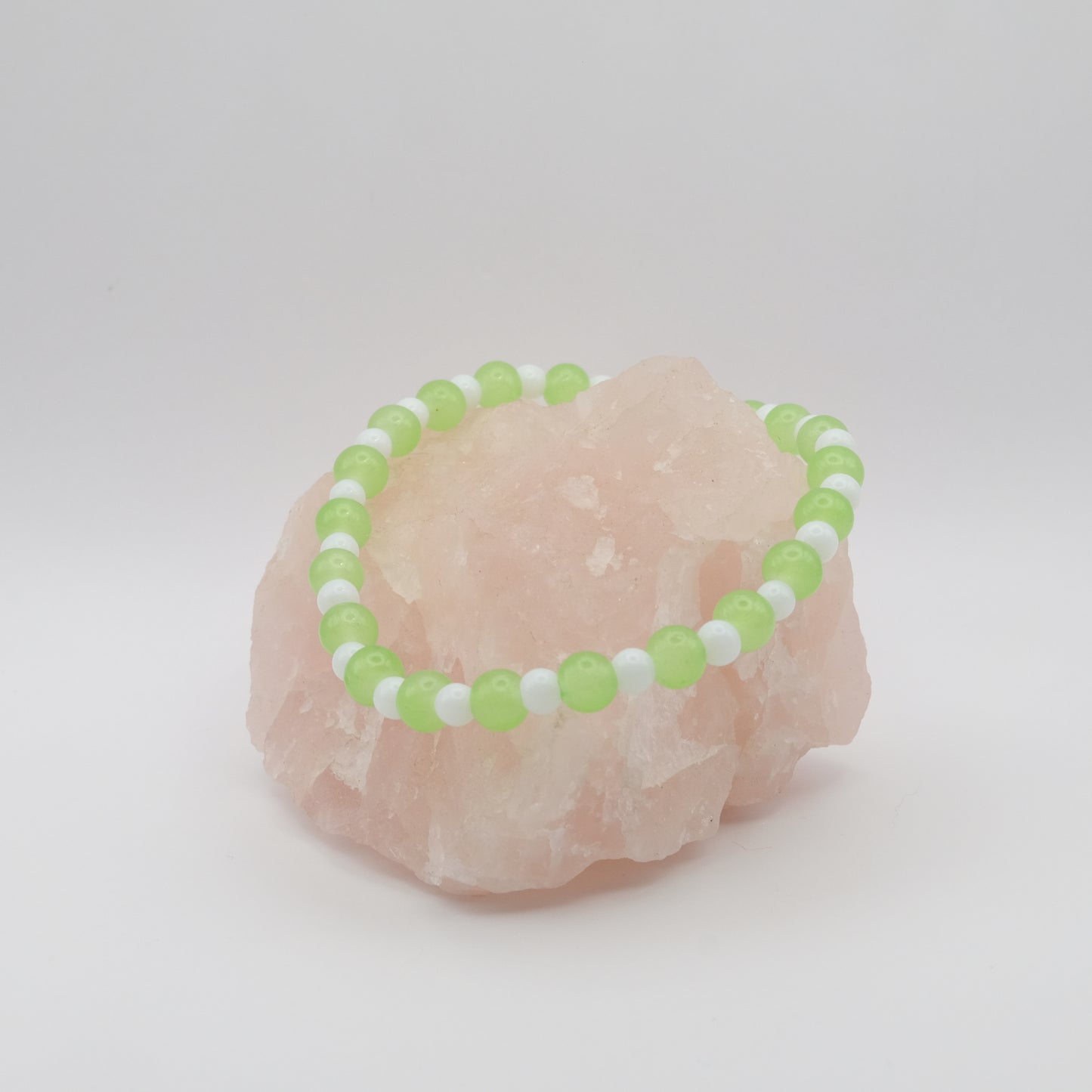 Green and white beaded bracelet on a pink stone with a white background