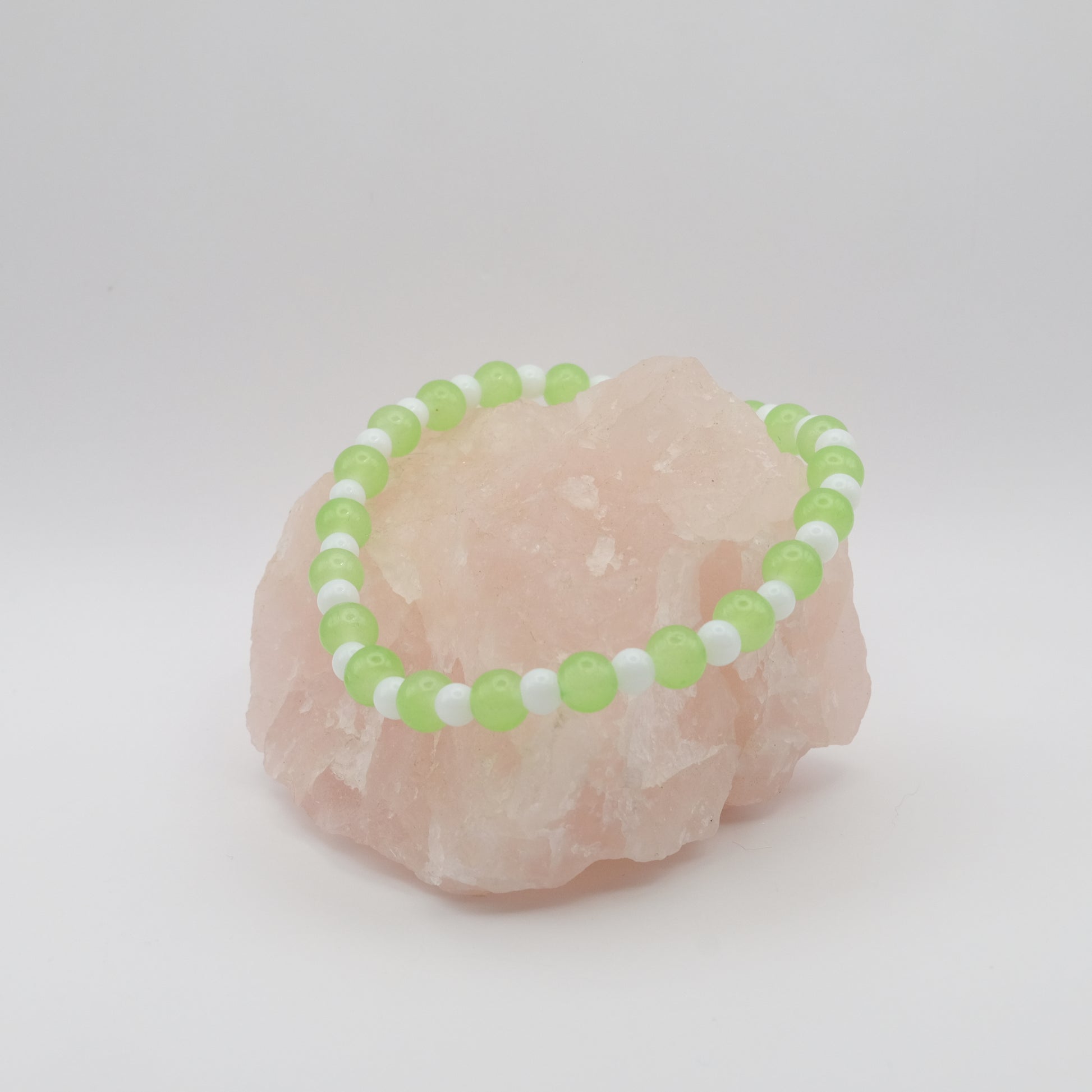 Green and white beaded bracelet on a pink stone with a white background