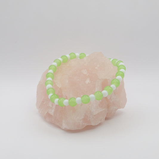 Green and white beaded bracelet on a pink stone with a white background