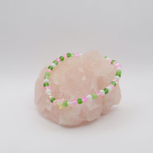 Beaded bracelet with green, pink, and white beads on a pink stone against a light gray background