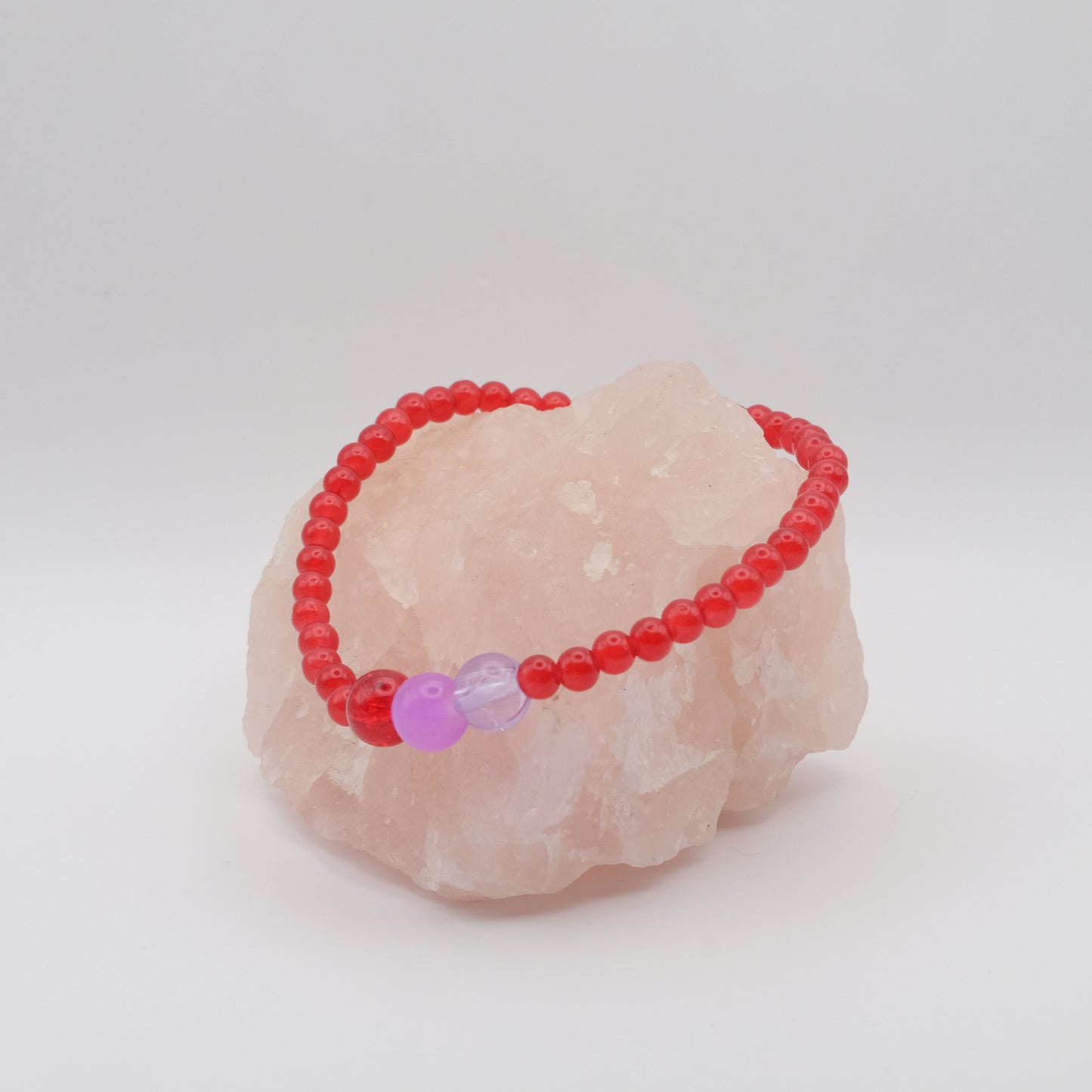 Red beaded bracelet with a pink bead on a pink stone against a white background