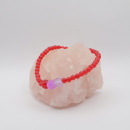 Red beaded bracelet with a pink bead on a pink stone against a white background