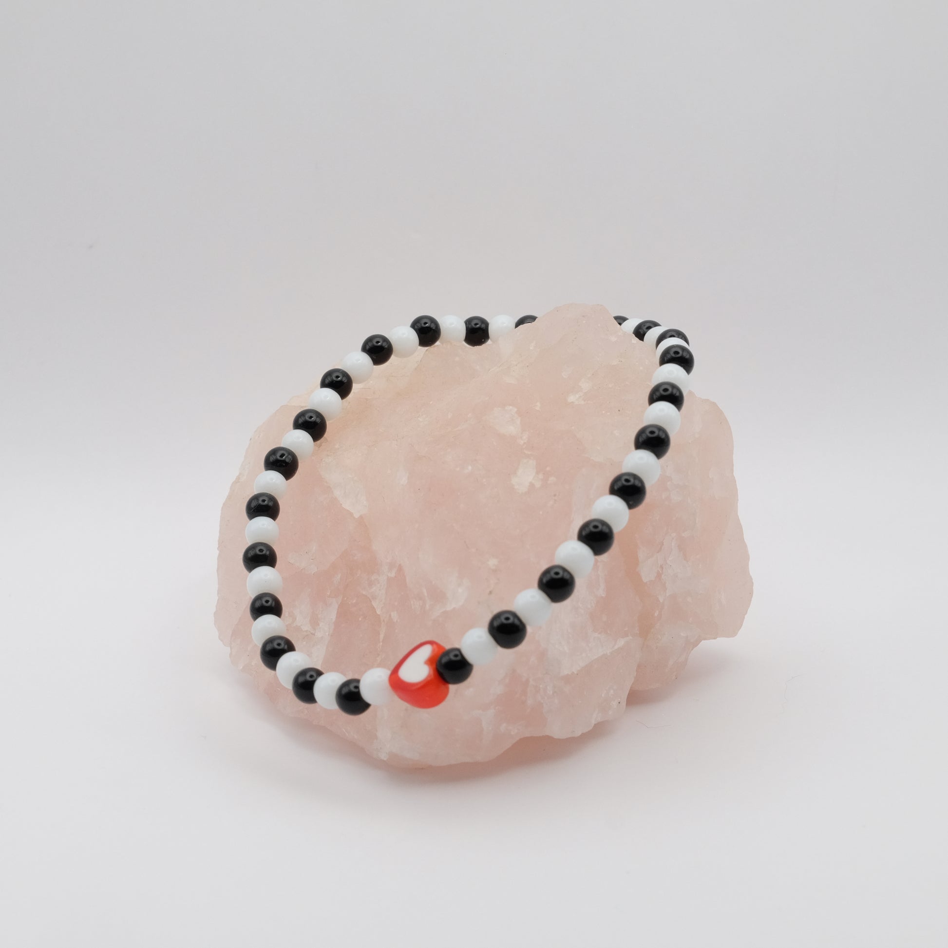Black and white beaded bracelet with a red charm on a pink stone against a white background