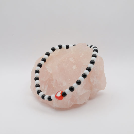 Black and white beaded bracelet with a red charm on a pink stone against a white background