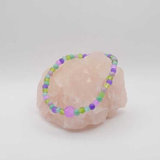 Beaded bracelet with purple and green beads on a pink stone against a white background