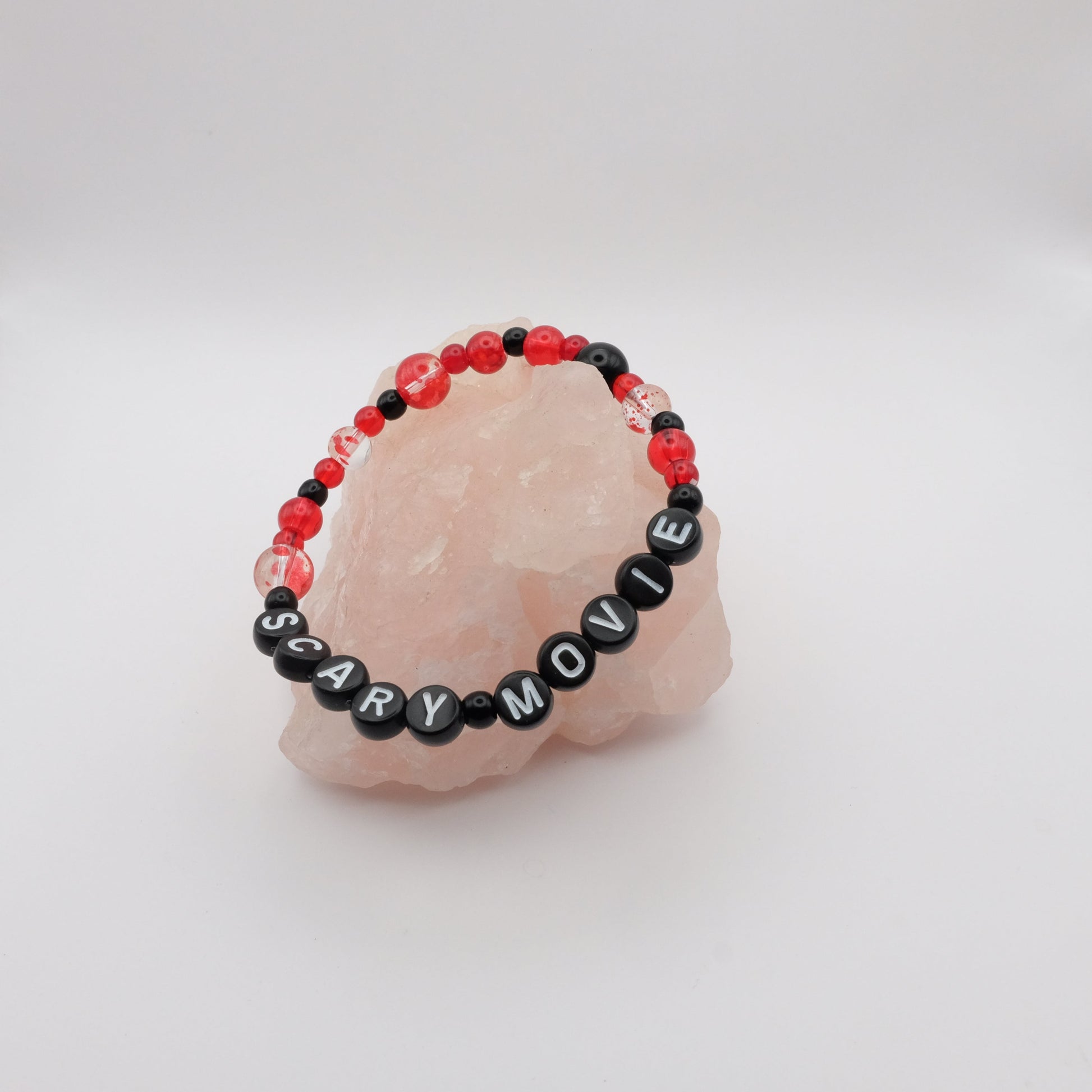 Bracelet with 'SCARY MOVIE' beads on a pink stone with a white background