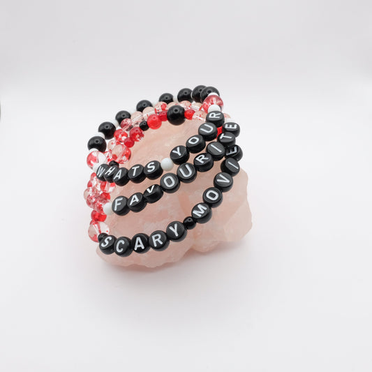 Black beaded bracelets with text on a pink stone against a white background