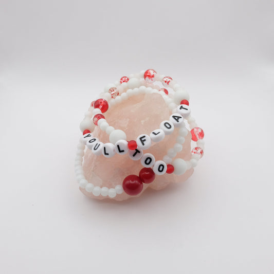 Beaded bracelets with red and white beads on a pink stone with 'YOU'LL FLOAT TOO' text.