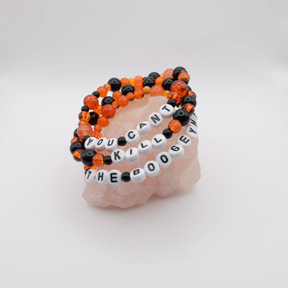 Stack of black  and orange beaded bracelets with letter beads spelling "YOU CANT KILL THE  BOOGEYMAN" on a white background