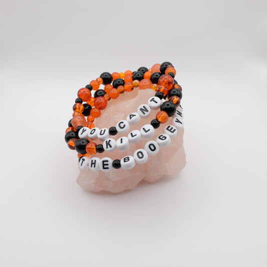 Stack of black  and orange beaded bracelets with letter beads spelling "YOU CANT KILL THE  BOOGEYMAN" on a white background