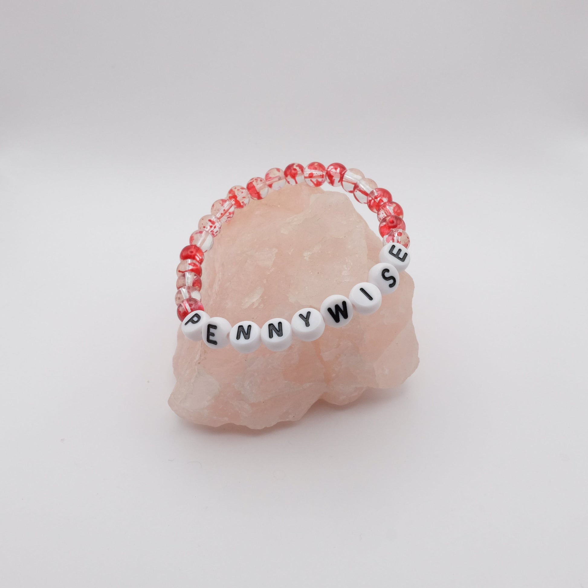 Pink stone with a beaded band labeled 'PENNYWISE' on a white background