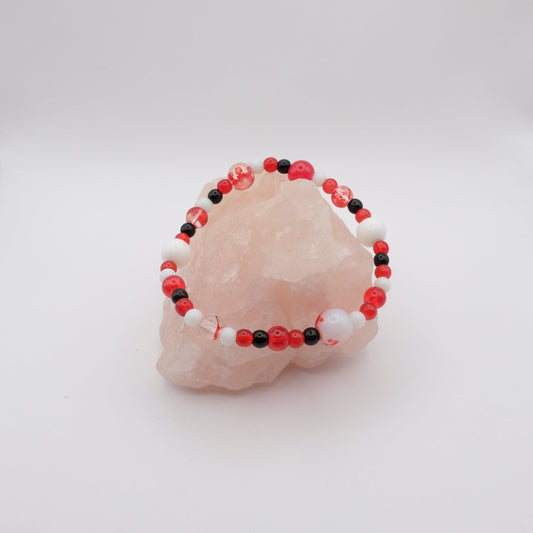 Beaded bracelet with red, black, and white beads on a pink stone against a white background