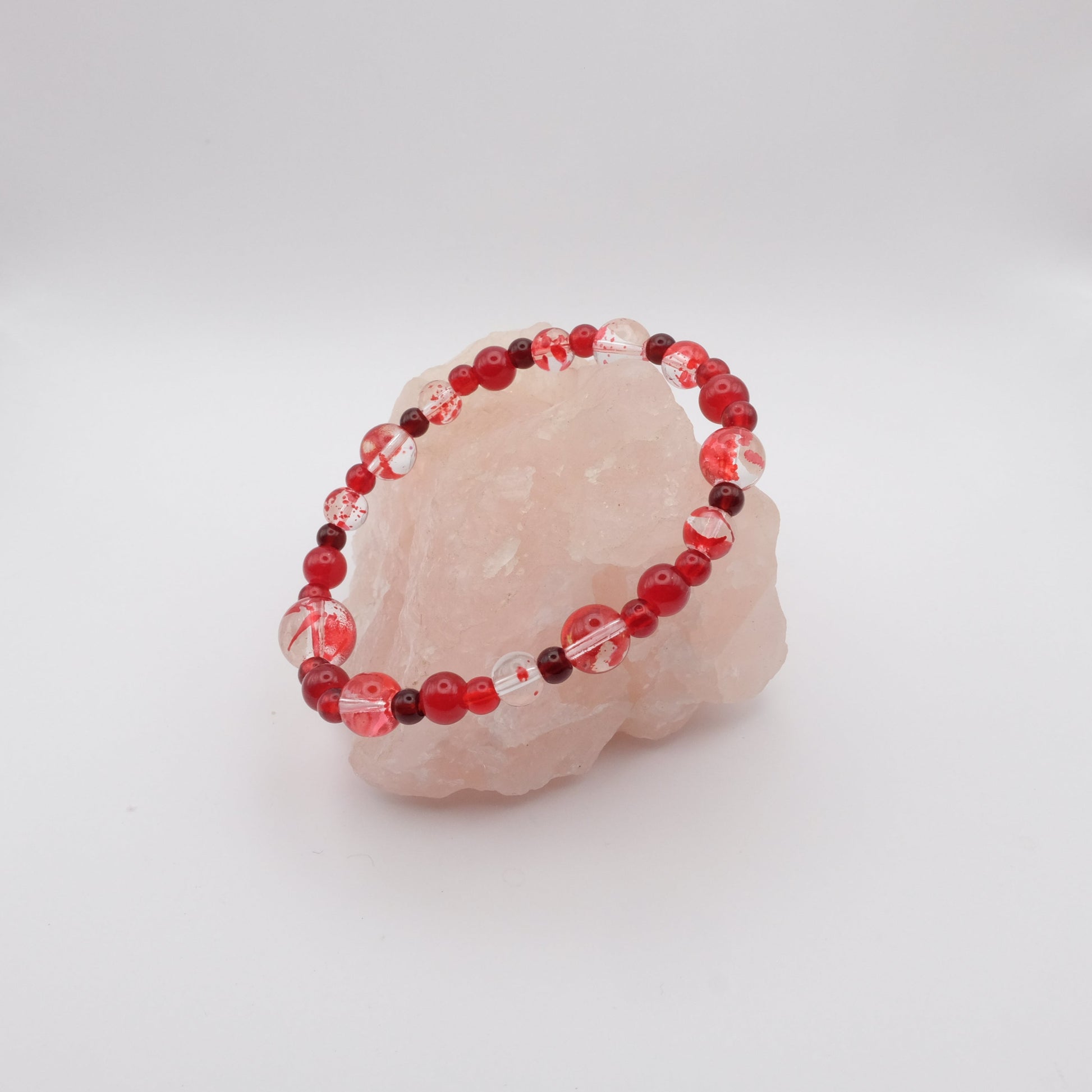 Beaded bracelet with red and clear beads on a pink stone against a white background