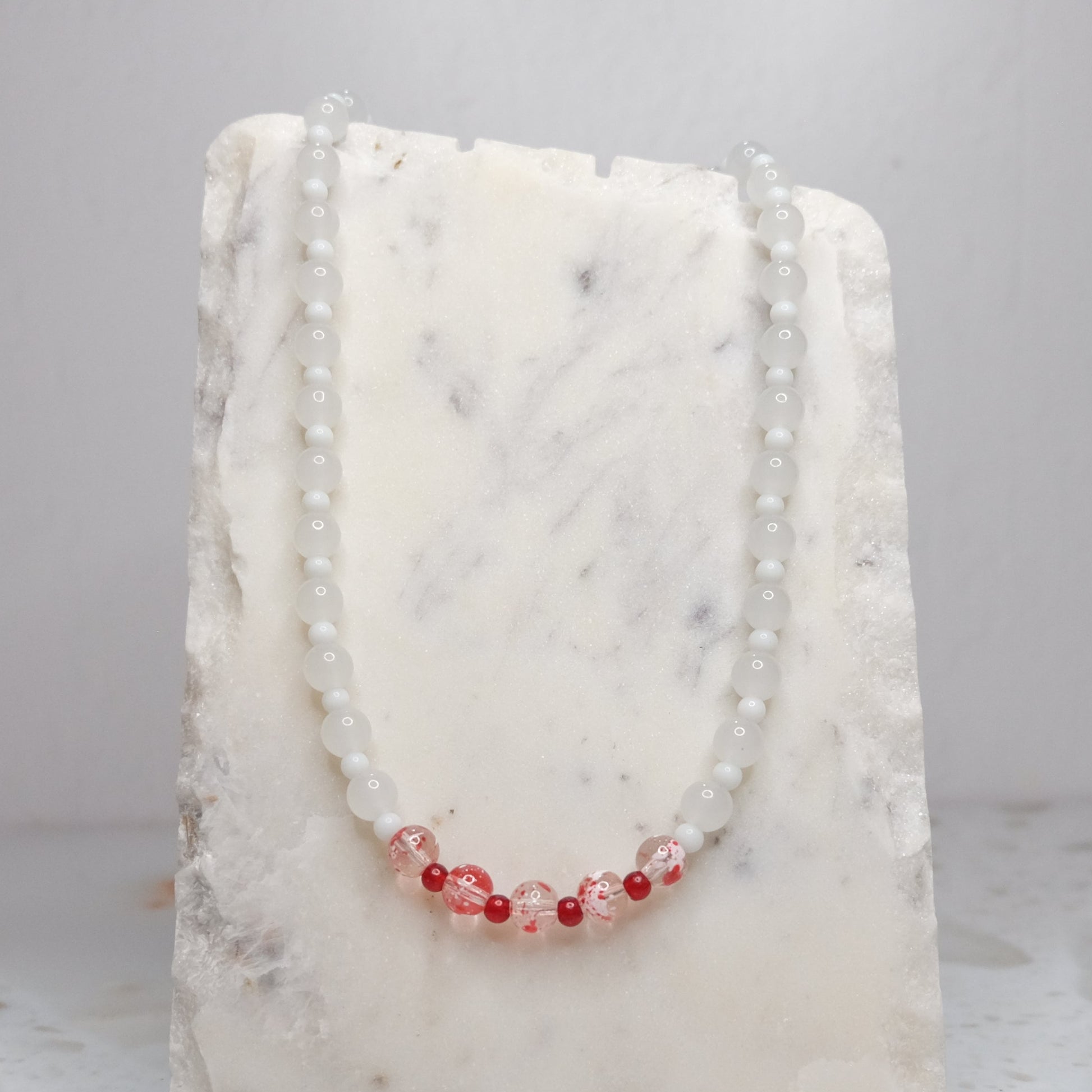 Necklace with white and red beads on a white stone surface