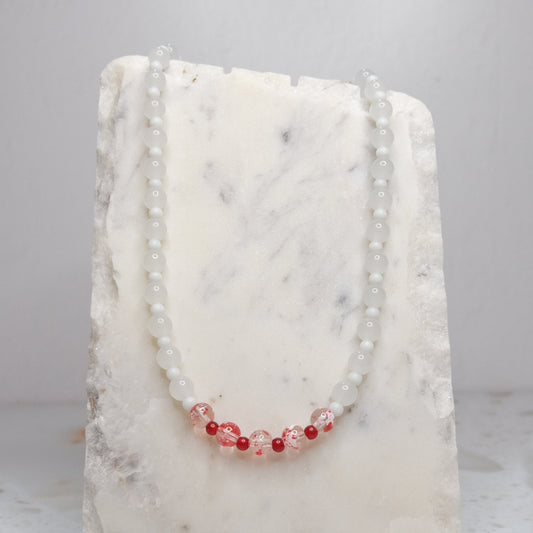 Necklace with white and red beads on a white stone surface